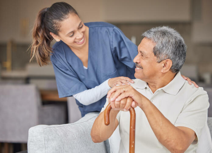 Healthcare, kindness and support with nurse helping elderly patient in assisted living home, smile and content. Happy senior man bonding with a friendly caregiver, talking and laugh together on sofa