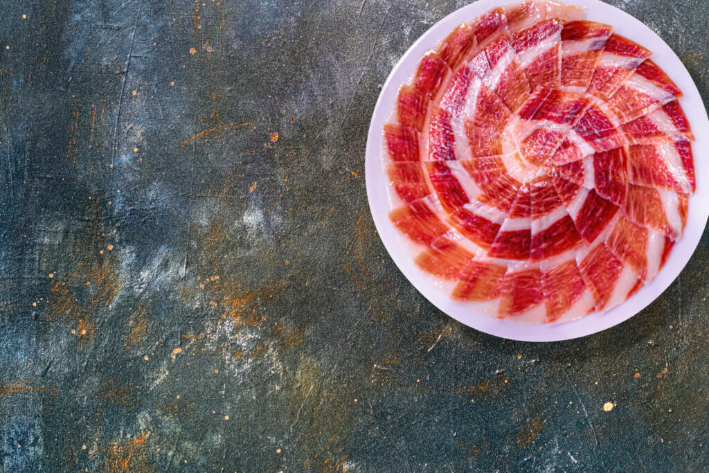 Iberian ham split in a spiral and presented on a plate with a dark galactic background