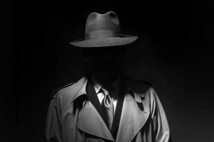 Man posing in the dark with a fedora hat and a trench coat, 1950s noir film style character