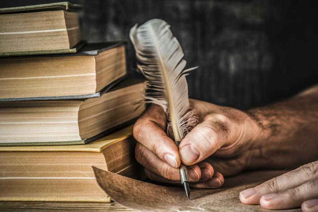 Man writing an old letter. Old quill pen, books and papyrus scroll on the table. Historical atmosphere.