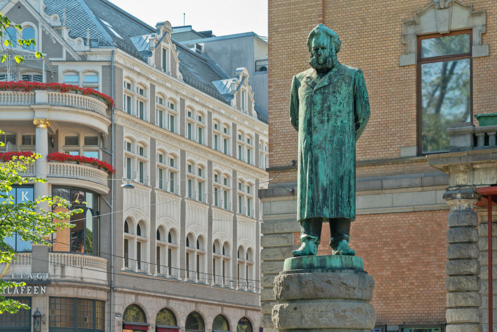 Oslo, Norway - June 29, 2022: Statue of Norwegian dramatist Henrik Ibsen outside the national theater in Oslo (Nationaltheatret). The statue was sculpted by artist Stephan Sinding and erected in 1899, the same year the National Theatre was built and had its first performance. The life-size statue of Ibsen has him standing with both hands behind his back and with the left hand cupped in the right hand.