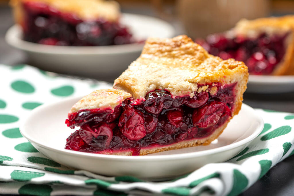 Piece of homemade cherry pie on a white plate close-up. Selective focus, dark background.