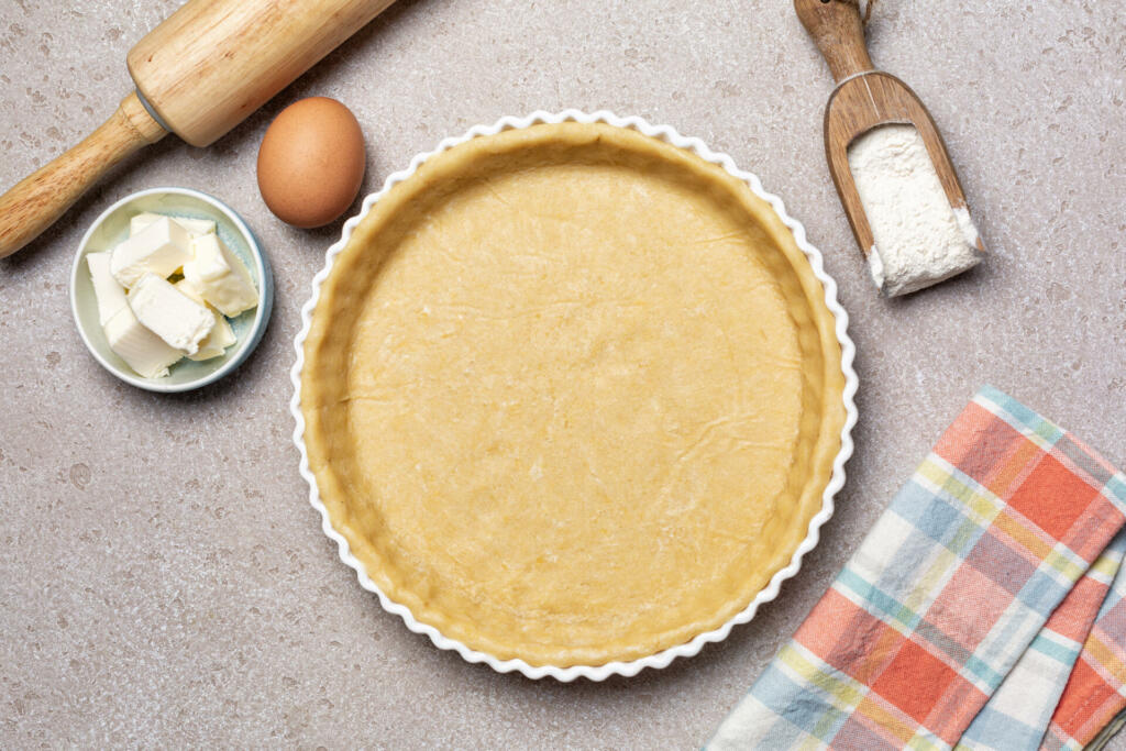 Raw, unbaked butter pie crust with ingredients for recipe, ehh, flour, butter, homemade pie dough. Top view.