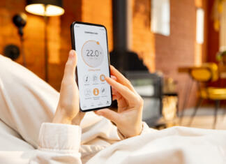 Nove funkcije na področju pametnega doma (VIDEO) Woman holding phone with running smart home application for heating temperature control, while lying relaxed at home. Close-up on device screen