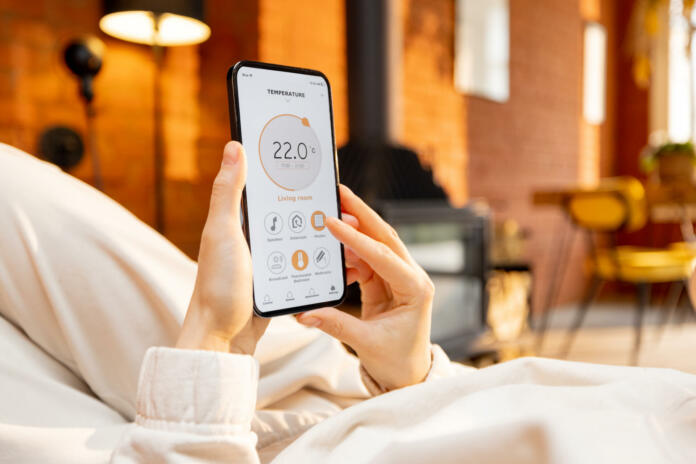 Woman holding phone with running smart home application for heating temperature control, while lying relaxed at home. Close-up on device screen