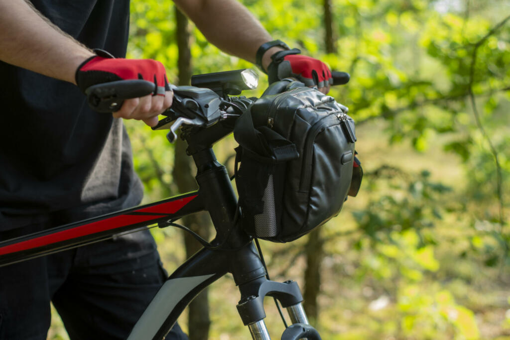 A cyclist in gloves near a mountain bike with a bag on the handlebars