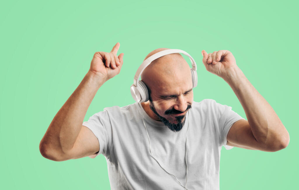 Bald man listening and enjoy the music and dancing on green background. Entertainment, sound, bass and mood