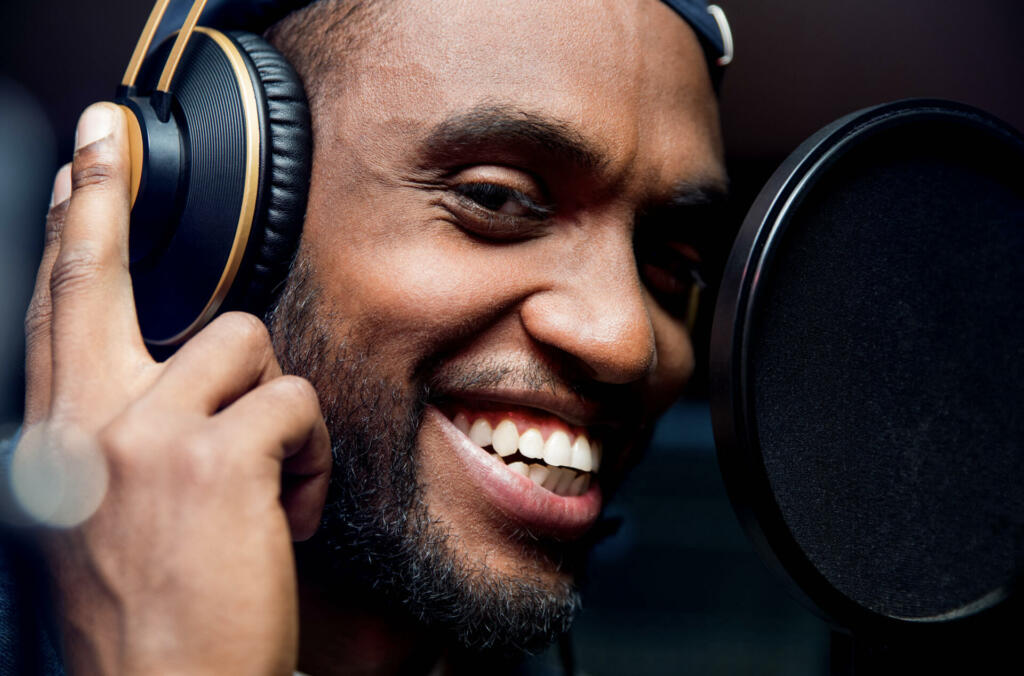 Bearded afro american man singing to microphone recording song in music studio production - Music, hobby and festival concept