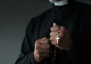 Close up of a priest holding rosary and praying with copy space