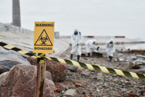 Close up of Warning Biohazard sign at ecological disaster site with people in protective suits, copy space