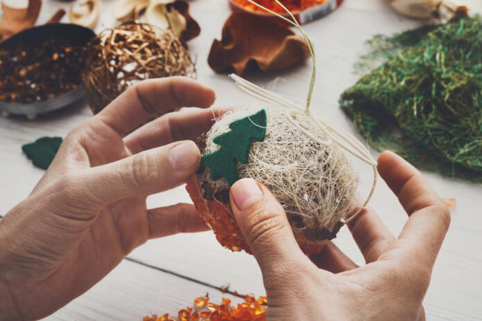 Creative diy craft hobby. Making handmade craft christmas ornaments and balls with felt spruce tree. Woman's leisure, holiday decorations. Closeup of female hands at white wood background