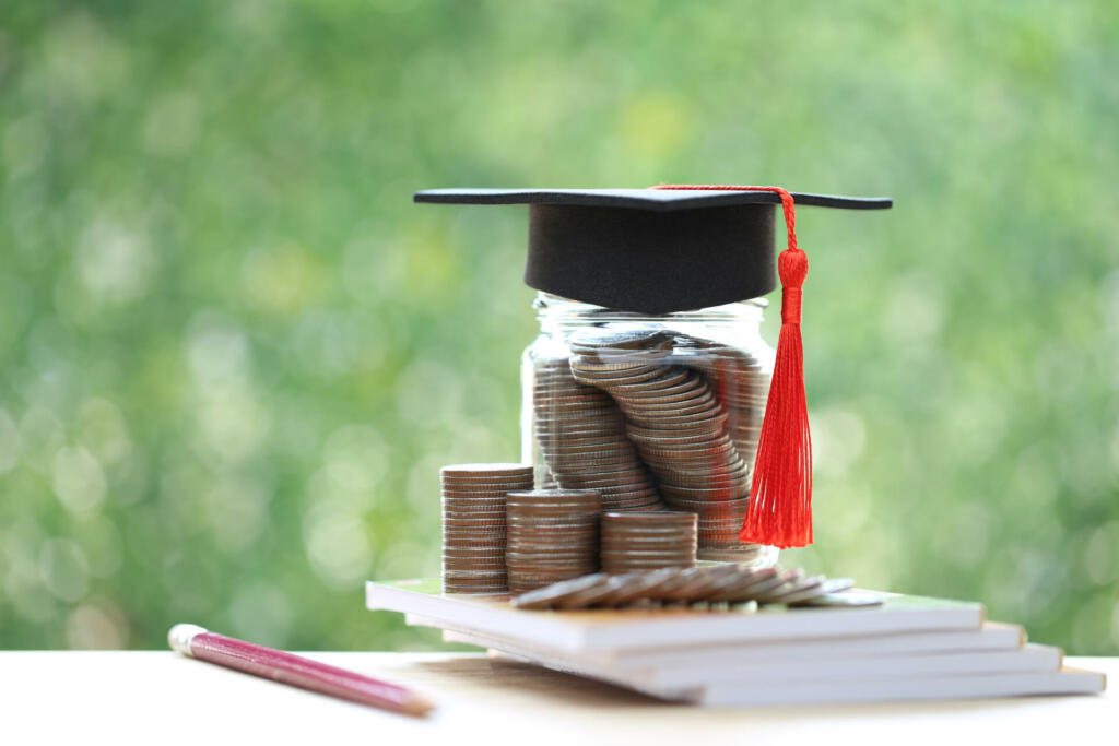 Graduation hat on coins money in the glass bottle on natural green background, Saving money for education concept