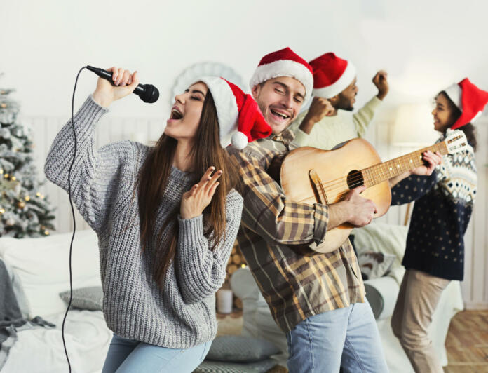 Happy couple playing on guitar and singing Christmas song at house party, copy space