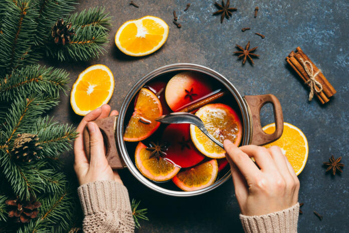 Hot Mulled wine cooking at home for happy christmas time. Red wine, orange, apple and spices - ingredients boiling in a pot on dark background. Warming new year and holiday drink, flat lay