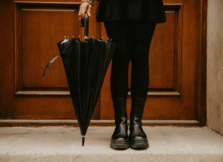 Kako izbrati idealen model ženskih škornjev Lower section of a woman in a black outfit holding a black umbrella