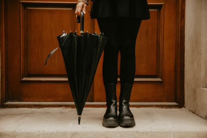 Lower section of a woman in a black outfit holding a black umbrella