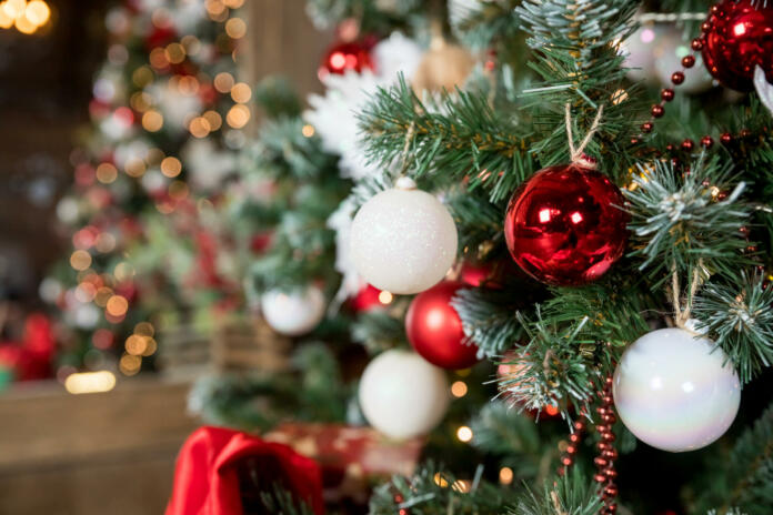 Magic glowing tree. Christmas home interior with Christmas tree. Red and white balls hanging on pine branches. Festive lights in the brick wall background.