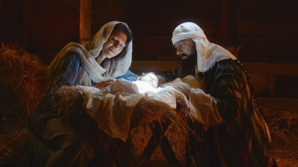 Mother Mary and Saint Joseph caressing baby Jesus sleeping in manger under bright divine light after birth in stable in Bethlehem