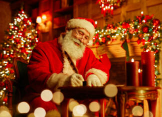 10 zanimivih dejstev o božiču Portrait of traditional Santa Claus writing letter by fireplace on Christmas eve and smiling, copy space