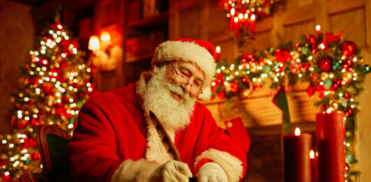 Portrait of traditional Santa Claus writing letter by fireplace on Christmas eve and smiling, copy space