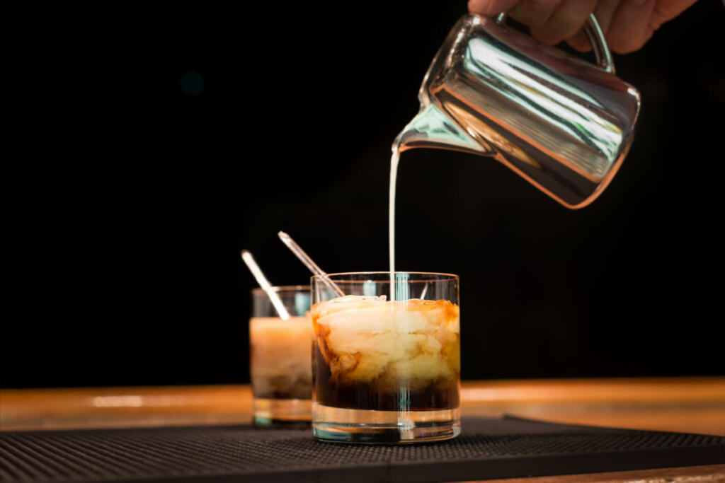 Preparation of white russian cocktails on the bar counter on rubber mat. Shallow DOF and marsala tonned