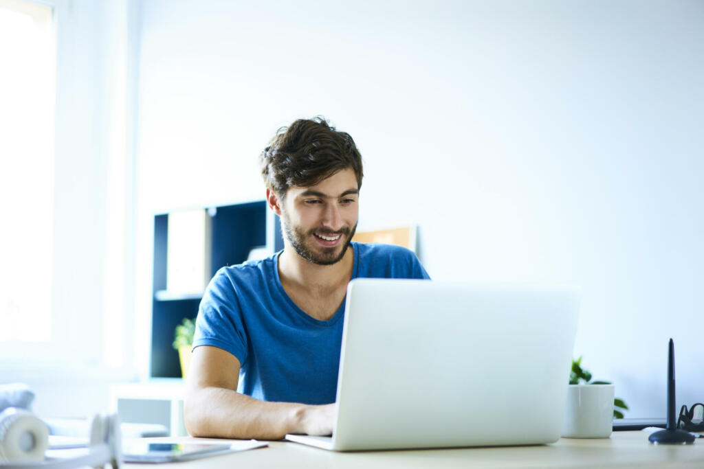 Smiling young man working on laptop in home office