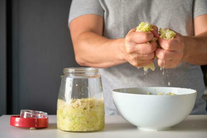 Unrecognizable man draining cabbage to prepare homemade sauerkraut or fermented cabbage.