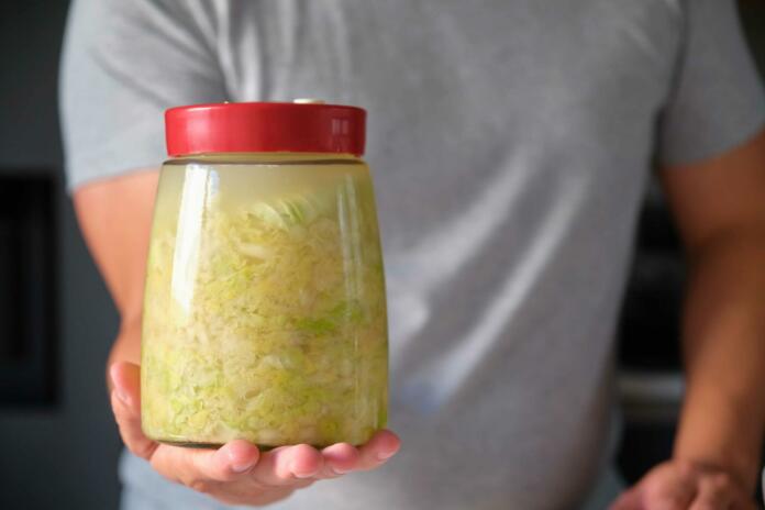 Unrecognizable man holding fermentation jar with homemade sauerkraut or fermented cabbage.