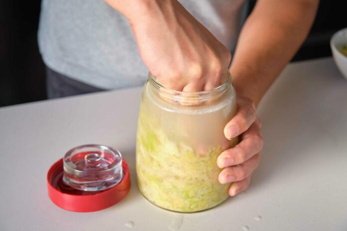 Unrecognizable man pressing down the cabbage to prepare homemade sauerkraut.