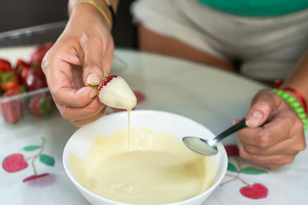 Woman dipping strawberries in white chocolate to cook a creative dessert.