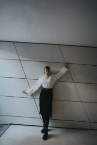 Young woman in a white turtleneck and black skirt leaning against the wall