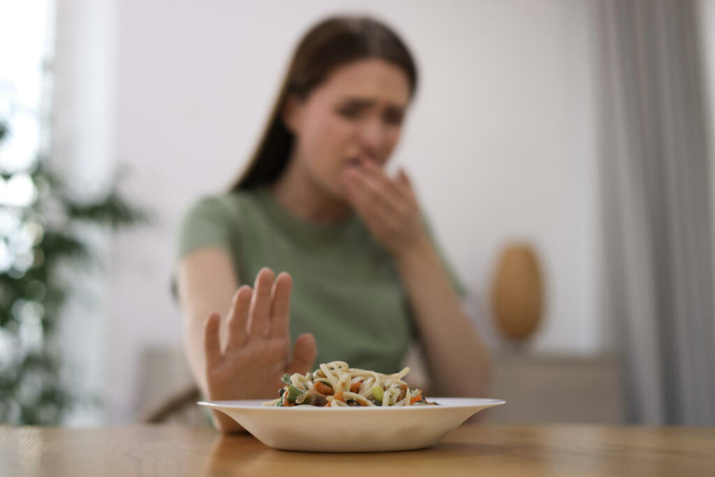 Young woman suffering from nausea at wooden table indoors, focus on food