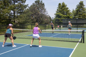 A pickleball player serves the ball during a game of doubles on a suburban court during summer.