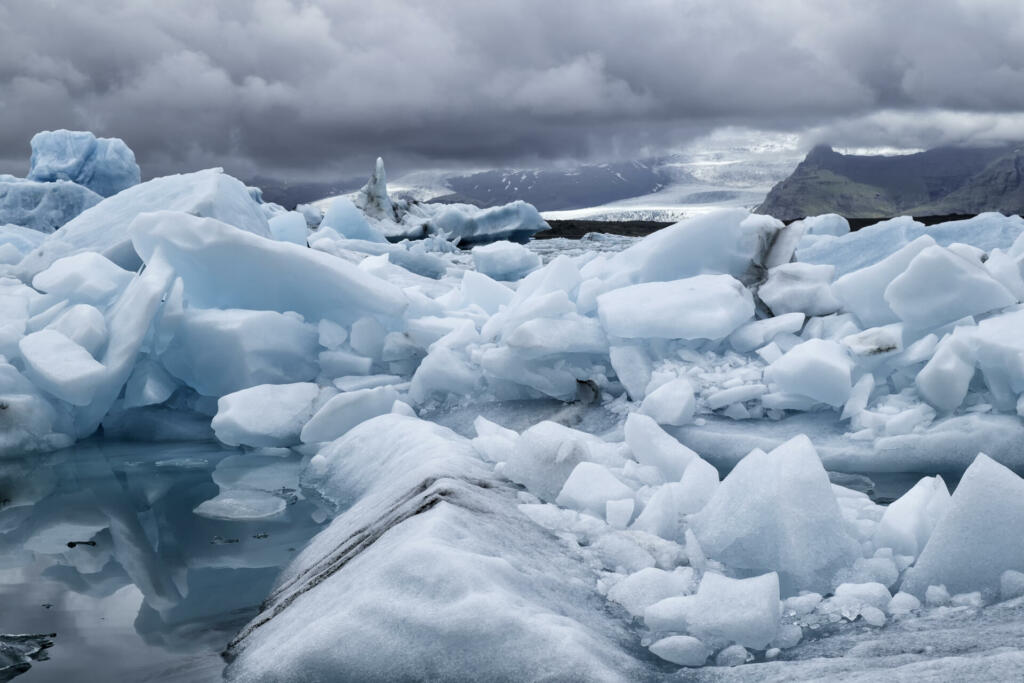 Blue icebergs floating the glacial lagoon in southeast Iceland in summer, blue water in the foreground with copy space and mountains and glacier in the background.