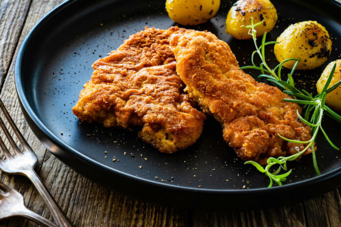 Breaded seared pork chop with fried potatoes and fresh vegetables on wooden table