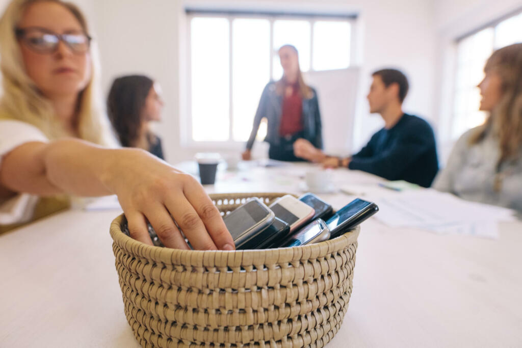 Female putting her cell phone in a basket while attending a board room meeting in her office. No cellphone zone at workplace meeting.