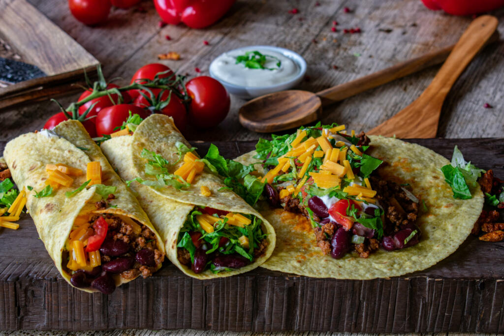 fresh and homemade burritos with minced meat and beans filling served on a wooden rustic board - mexican food - ready to eat