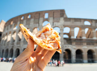 10 mest z najboljšo hrano na svetu Hand Holding Slice Of Italian Pizza Near Colosseum, Rome