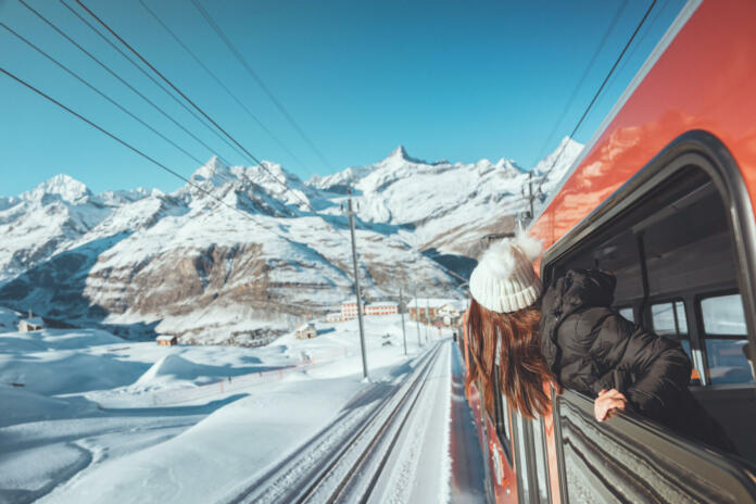 Happy woman traveler looks out from window traveling by train in beautiful winter mountains, Travel concept.