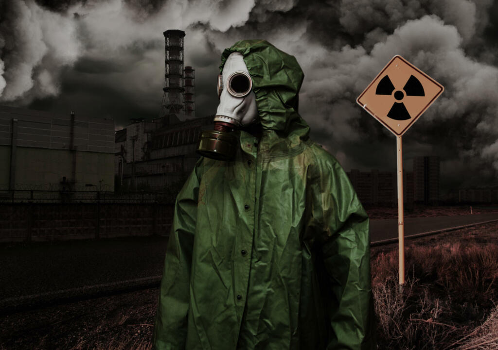 Man in gas mask and cloak of chemical protection on abandoned road in front of Nuclear station. Nuclear pollution concept