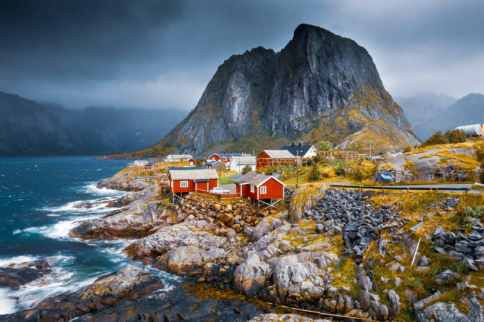 Norwegian fishing village with red houses. Landscape of the Lofoten Islands. Fjord under a dramatic cloudy sky. Northern seascape.