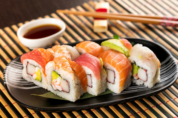 Set of rainbow uramaki sushi rolls with tuna, salmon and avocado, served in restaurant on bamboo mat