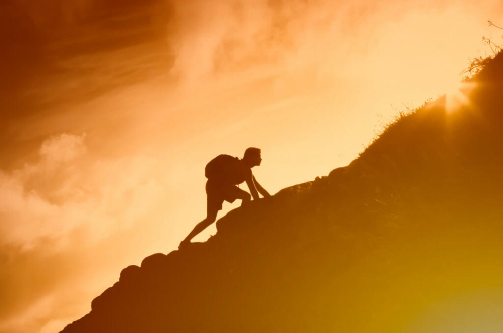 Silhouette of man climbing up a mountain