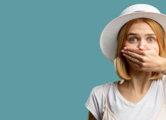 Zakaj smo skrivnostni? Speech freedom. Female rights. Scared woman in white closing mouth hand looking at camera isolated on blue copy space. Keep secret. Advertising background