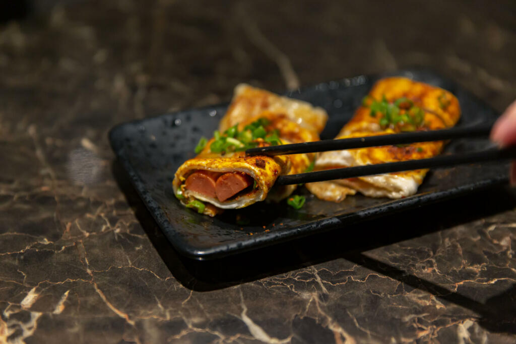 Tianjin-Style Jianbing Pancake with Sausage Filling and Spring Onion Topping, Served with Chopsticks, selective focus