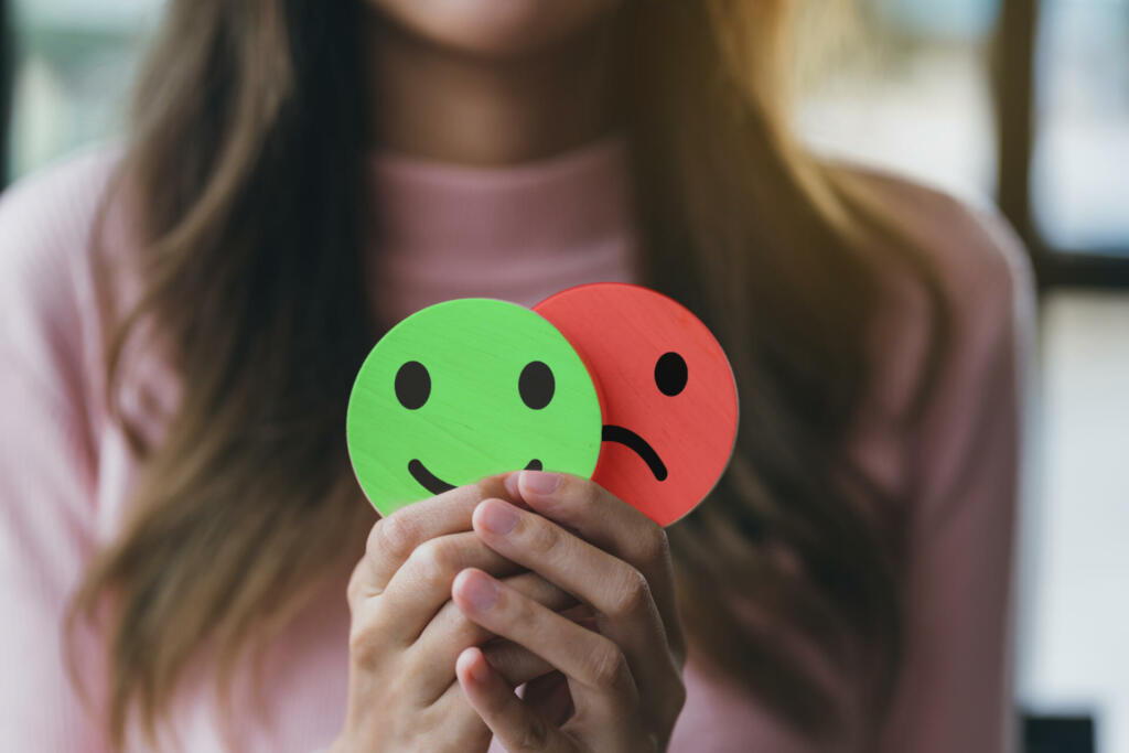 Woman Hands holding sad face hiding or behind happy smiley face, bipolar and depression, mental health concept, personality, mood change, therapy healing split concept.