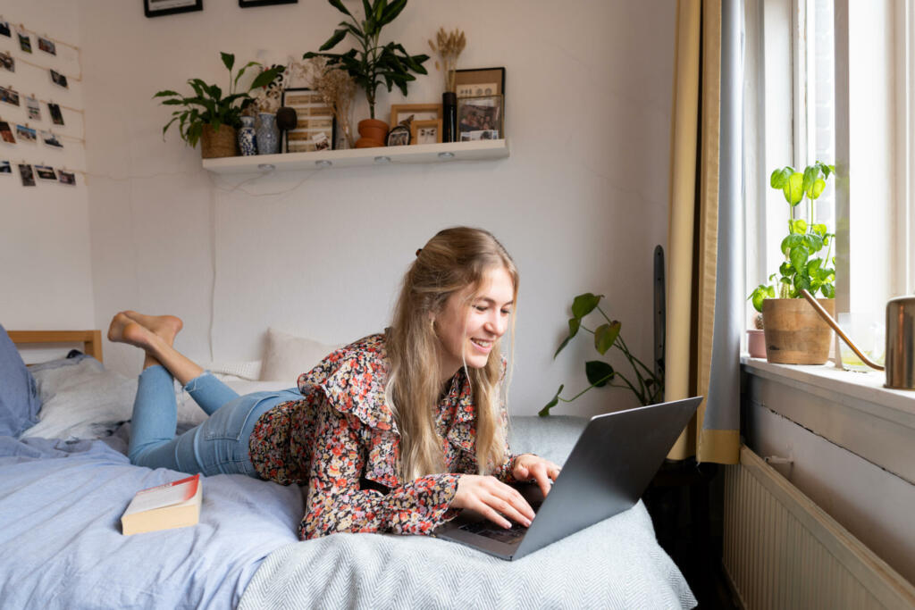 Young university student following lecture on her laptop on the bed