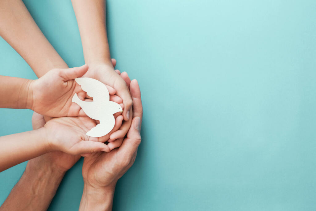 Adult and child hands holding white dove bird on blue background, international day of peace or world peace day concept, sustainable consumption, csr responsible business concept