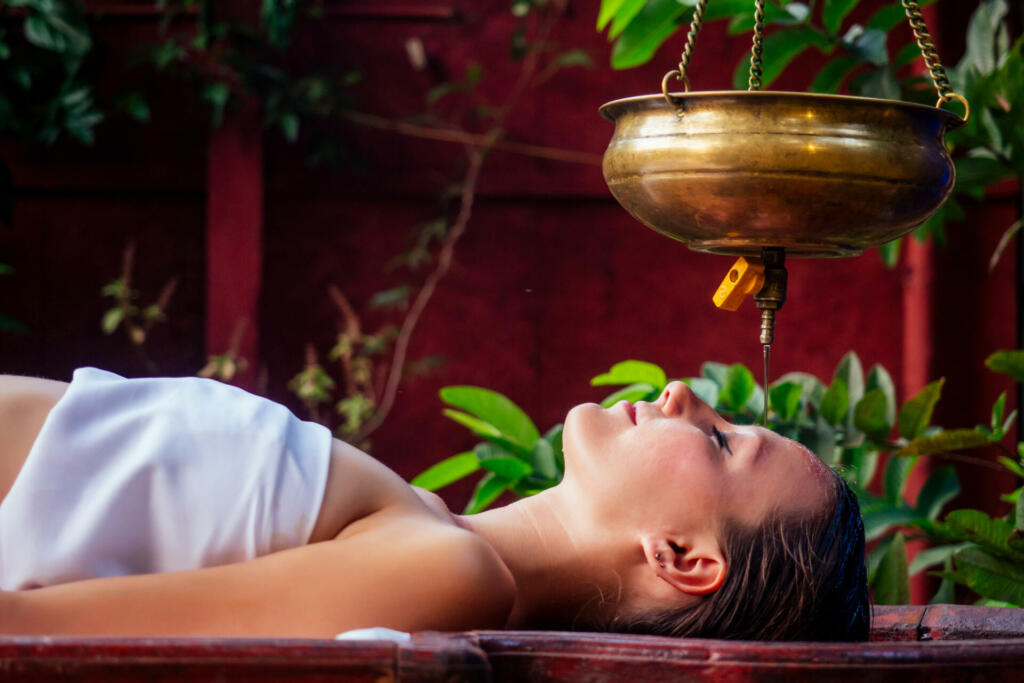 ayurveda massage alternative healing therapy.beautiful caucasian female getting shirodhara treatment lying on a wooden table in India salon