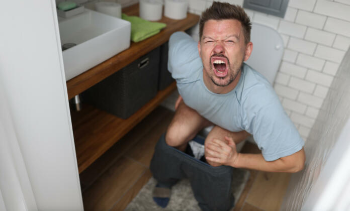 Man suffering from hemorrhoids screams on toilet in toilet. Internal hemorrhoids causes symptoms and treatment